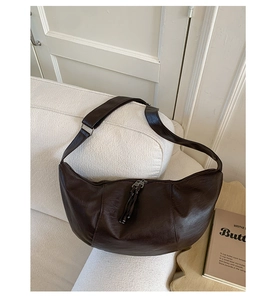 Detail of a dark brown hobo bag with leather texture and tassel zipper on a white sofa