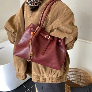 Détail du cabas en cuir bordeaux avec boucle dorée et breloque en perles ethniques