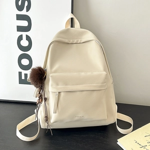 Detail view of cream faux leather backpack with textured finish and brown pompom charm