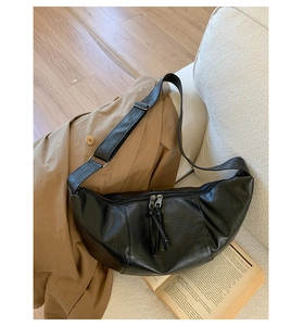 Detail of black crescent leather shoulder bag with tassels on casual trench coat