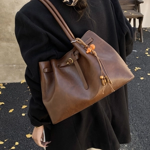 Détail du sac cabas vintage marron avec pompon en perles de bois sur une rue d'automne