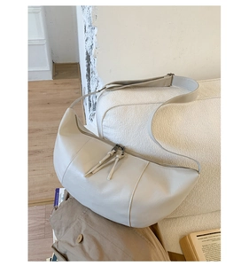Detail of off-white crescent bag with tassels and adjustable strap on a sofa
