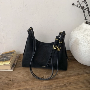 Detail of black suede hobo bag with gold metal buckle on a minimalist wooden surface