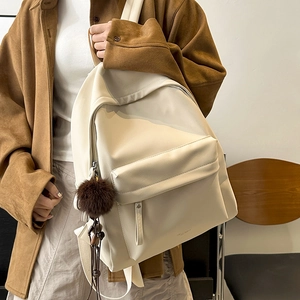 Close-up of cream PU leather backpack with side plush pendant on a female model