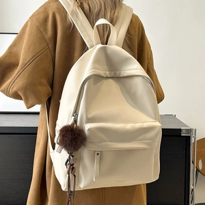 Detail of cream PU leather backpack with brown pompom charm on a wool coat