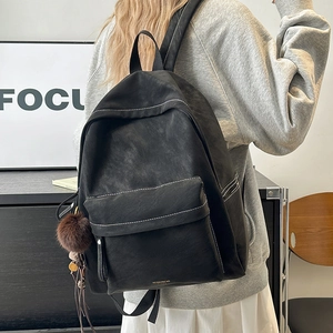 Detail of vintage black leather backpack with white contrast stitching and fur ball charm