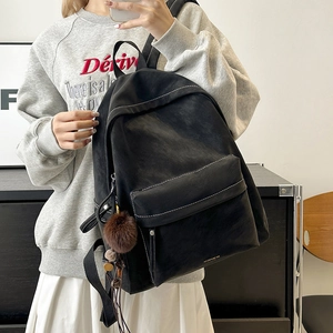 Detail of black faux leather backpack with white stitching and plush ball charm