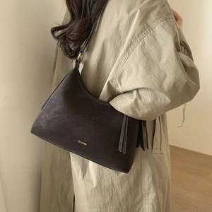 Detail view of deep brown matte leather hobo bag with gold logo on olive trench coat