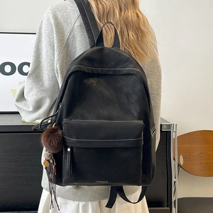 Detail of black backpack with contrast stitching and decorative furry ball charm