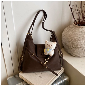 Detail of dark brown faux leather hobo bag with cute teddy bear charm on luggage