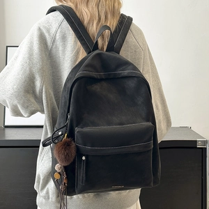 Close-up of black backpack with white contrast stitching and brown fluffy charm detail