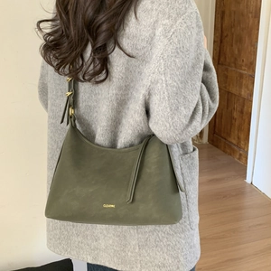 Detail of moss green matte leather shoulder bag with adjustable strap on grey coat