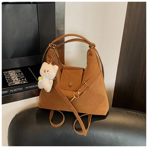 Detail of a brown faux suede hobo bag featuring a white bear plush charm and shoulder strap