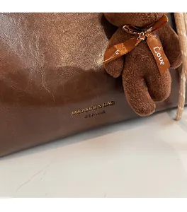 Close-up of brown litchi leather tote with gold logo and plush bear charm detail