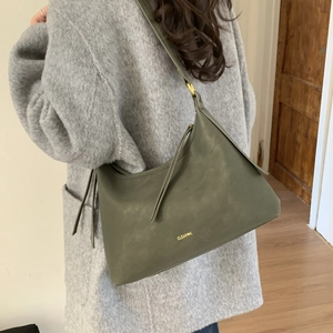 Detail of dark olive green leather tote bag with gold logo shown on model's shoulder
