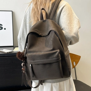 Detail of dark brown leather backpack featuring white stitching and plush tassel charm