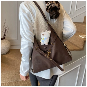 Detail of dark brown leather tote bag with white plush bear charm and golden hardware