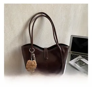 Detail of dark brown leather tote bag with a cute plush bear charm on a desk
