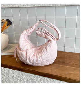 Detail of pink heart-quilted nylon crescent bag on a wooden table against a white wall