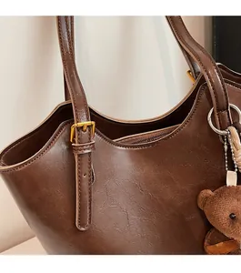 Detail of dark brown tote featuring adjustable leather strap with gold buckle and bear charm