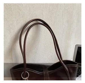 Detailed close-up of slim shoulder straps with silver metal rings on a brown tote bag