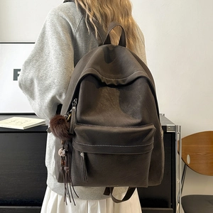 Detail of vintage brown leather backpack with contrast stitching and plush ball charm