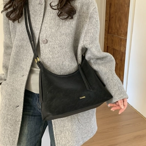 Detail view of the black matte hobo bag texture and gold buckle on a gray coat outfit