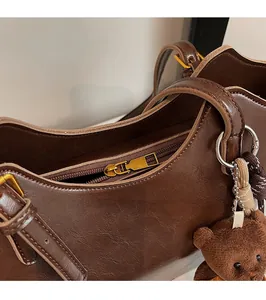 Detail of smooth metal zipper and brown plush bear charm on a dark leather tote bag