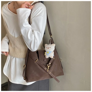 Detail of a dark brown tote bag with flip cover and a cute white teddy bear pendant