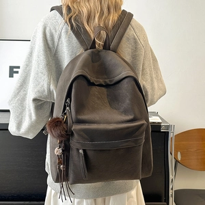 Detail of dark brown leather backpack with contrast stitching and decorative fur ball charm