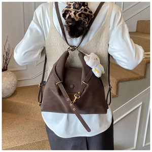Detail of dark brown matte tote bag with gold metal hooks and white plush bear charm
