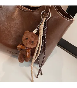 Detail of soft brown plush bear charm with 'Love' ribbon on a leather tote bag