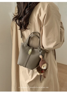 Chic taupe pebbled leather bucket bag with cute bear charm worn on a long coat