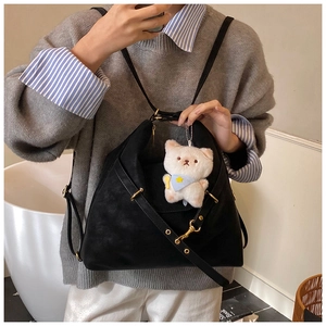 Detail of black tote bag with matte texture, gold metal buckles and white cat plush charm