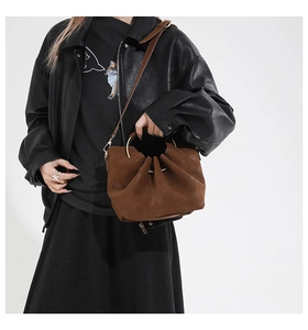 Brown pleated bucket bag with gold circular handle and adjustable shoulder strap worn by a model