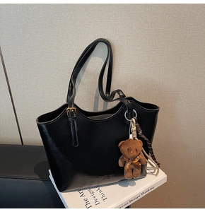 Detail of a black large tote bag with metallic buckle and cute brown bear pendant charm