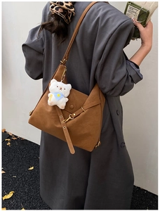 Brown matte leather tote bag with stylish teddy bear charm in an autumn street setting