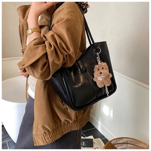 Large black leather tote bag with brown plush bear charm shown in a minimalist outfit