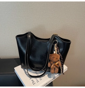Detail of a large black tote bag with glossy finish and cute brown plush bear charm