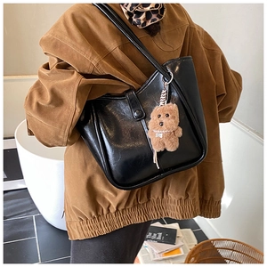Detail view of black faux leather shoulder bag with plush bear charm and buckle strap