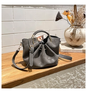 Détail du sac seau gris avec poignée ronde en métal doré sur surface en bois