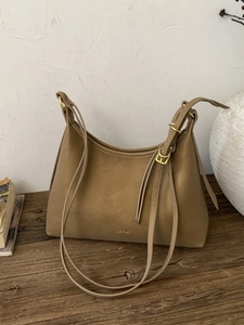 Retro khaki dumpling bag with golden CLEAR M logo on a vintage wooden surface