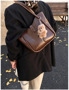 Detail of dark brown leather shoulder bag with plush bear charm in an autumn setting