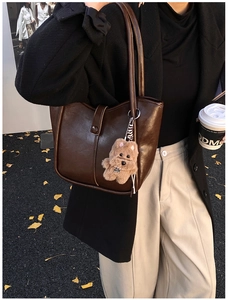 Brown glossy leather bucket bag with cute plush bear charm on a city street