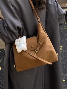 Large brown hobo bag with teddy charm shown on a grey coat in an outdoor street setting