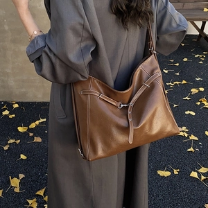 Detail einer großen braunen Shopper-Tasche mit Kontrastnähten und Schnalle am grauen Mantel