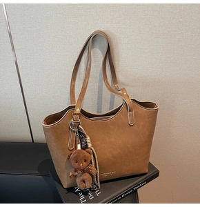 Detail of a brown leather tote bag featuring a plush teddy bear charm and soft textures