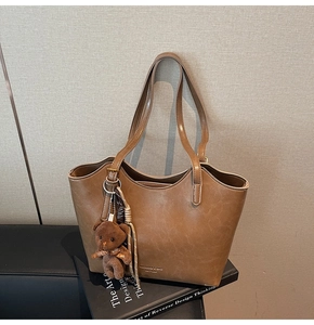Detail of vintage brown leather tote bag with gold logo and cute teddy bear charm