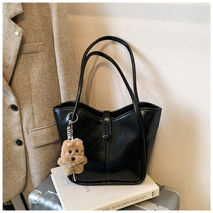 Close-up of black glossy bucket bag with plush puppy charm and minimalist strap detail