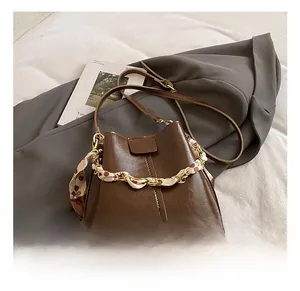 Close-up of brown bucket bag with silk scarf wrapped chain on grey fabric
